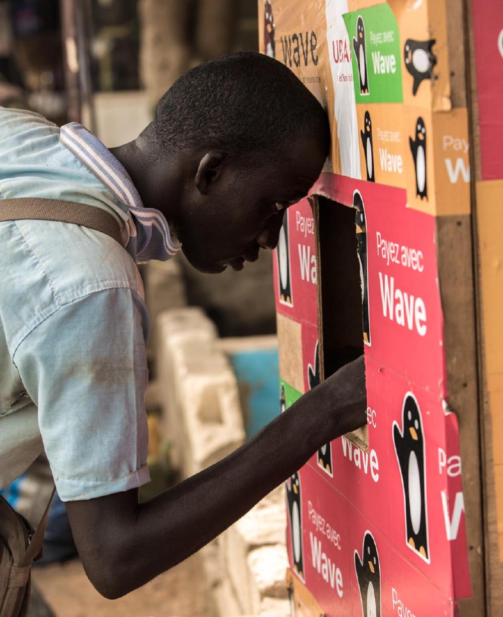 A man peering into a Wave agent kiosk covered in Wave stickers